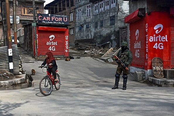 A girl rides a bicycle as policeman stands guard during curfew in Srinagar | - gettyimages